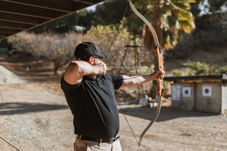 pexels-photo-6669179-6669179 Adult male archer practicing with a recurve bow at an outdoor range on a sunny day.
