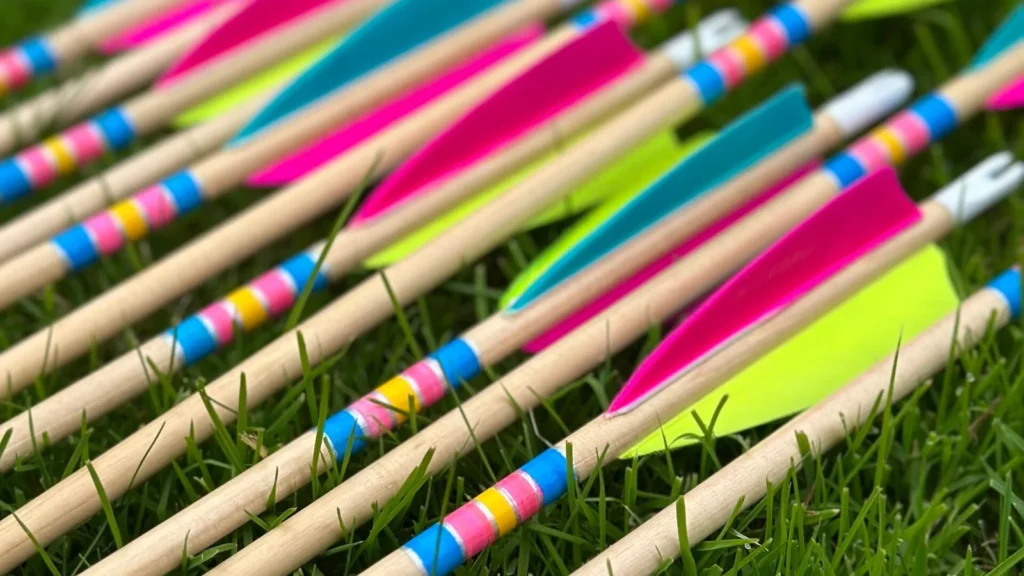 Finished wooden arrows with brightly coloured fletchings laid on grass