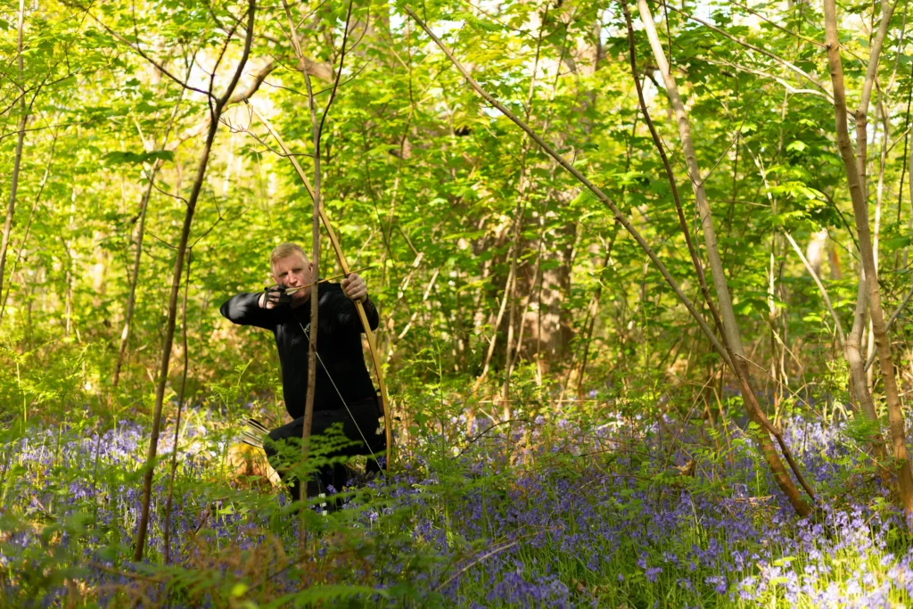 Traditional archers shooting among bluebells in sunlit woodland